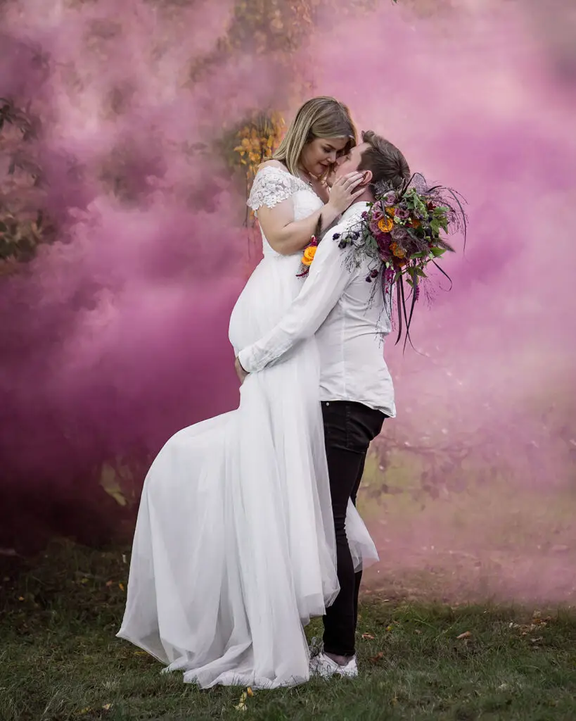 Brudgum lyfter bruden bland rosa rökmoln.
