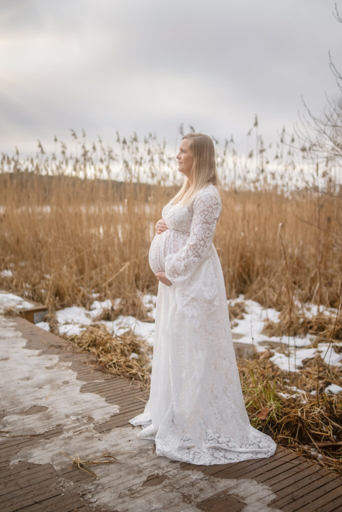 Gravid kvinna vid en brygga i vit spetsklänning