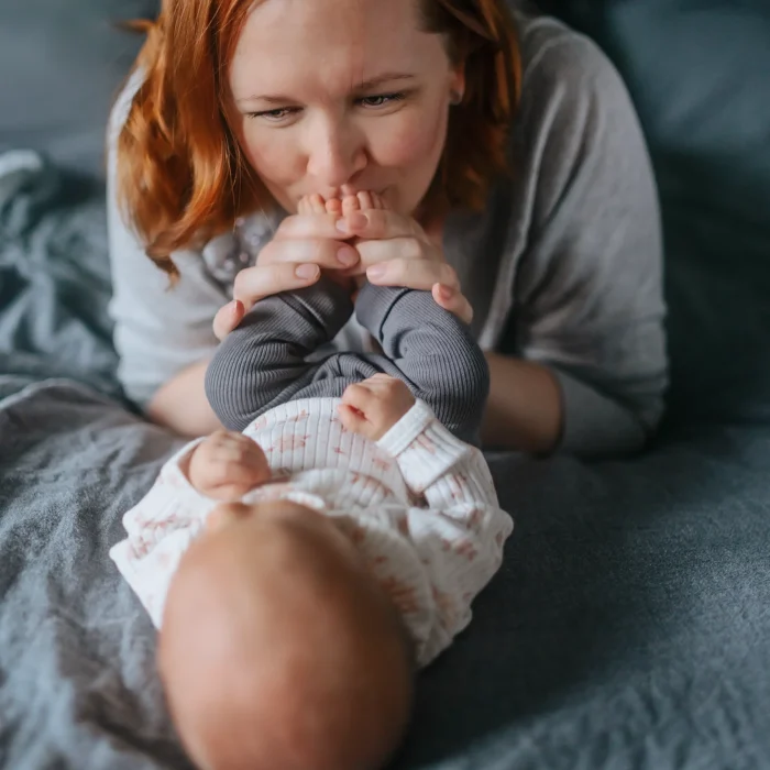 Mammafotografering inomhus där mamma pussar sin bebis fot